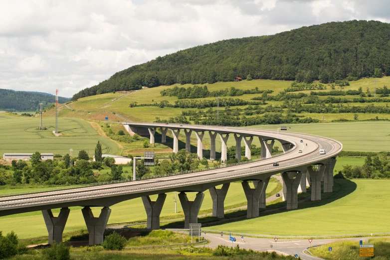 a large long bridge over a lush green field, a picture, by Thomas Häfner, shutterstock, car on highway, concrete pillars, norway, work of art