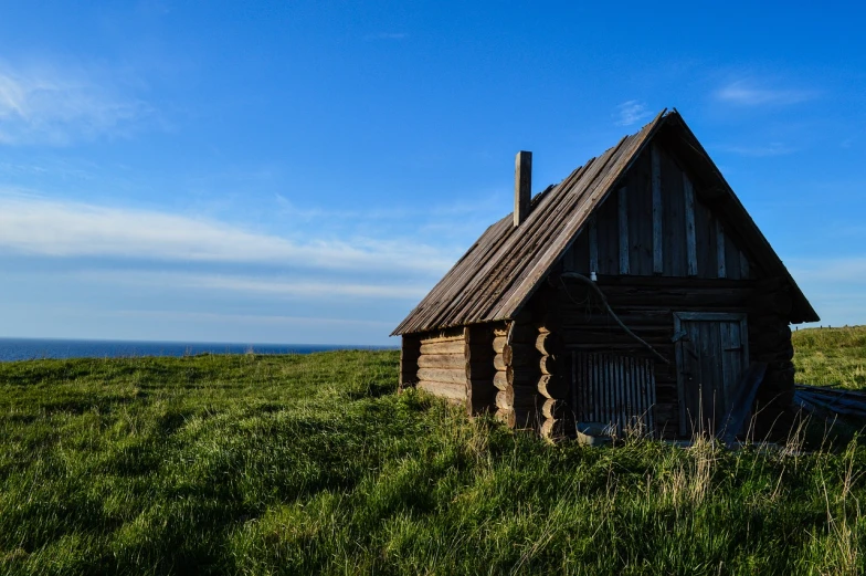 a small wooden cabin sitting on top of a lush green field, a stock photo, by Alexander Bogen, shutterstock, old cowboy in the arctic, built around ocean, shot on leica sl2, old abandoned house