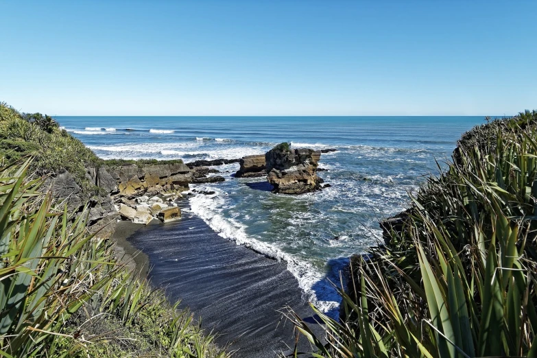 a body of water sitting on top of a lush green hillside, by Peter Churcher, shutterstock, hurufiyya, rocky beach, sunny day at beach, black sand, bulli