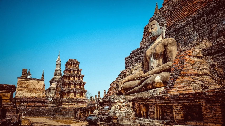 a statue of a person sitting in front of a building, a statue, beautiful ancient ruins behind, buddhist art, featured, evan lee