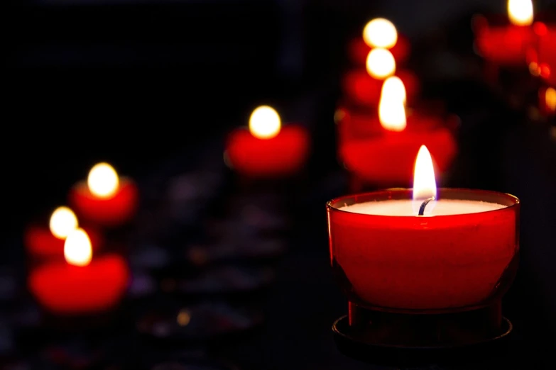 a group of red candles sitting on top of a table, a picture, shutterstock, with a black dark background, holy light, dlsr photo, in a row