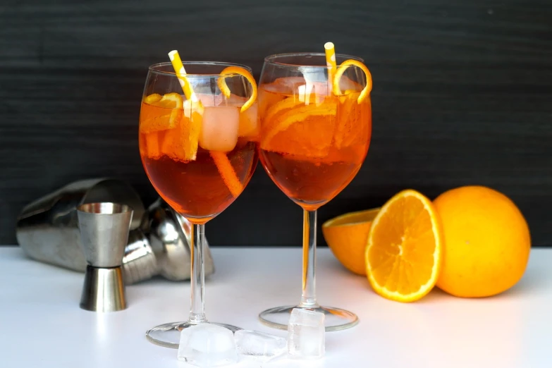 a couple of wine glasses sitting on top of a table, inspired by Carlo Martini, pexels, orange slices, tall iced tea glass, paolo veronese style, profile pic