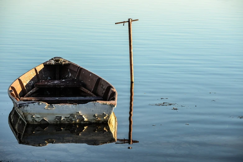a boat sitting on top of a body of water, a photo, by Richard Carline, shutterstock, weathered, water reflection, dingy, half body photo