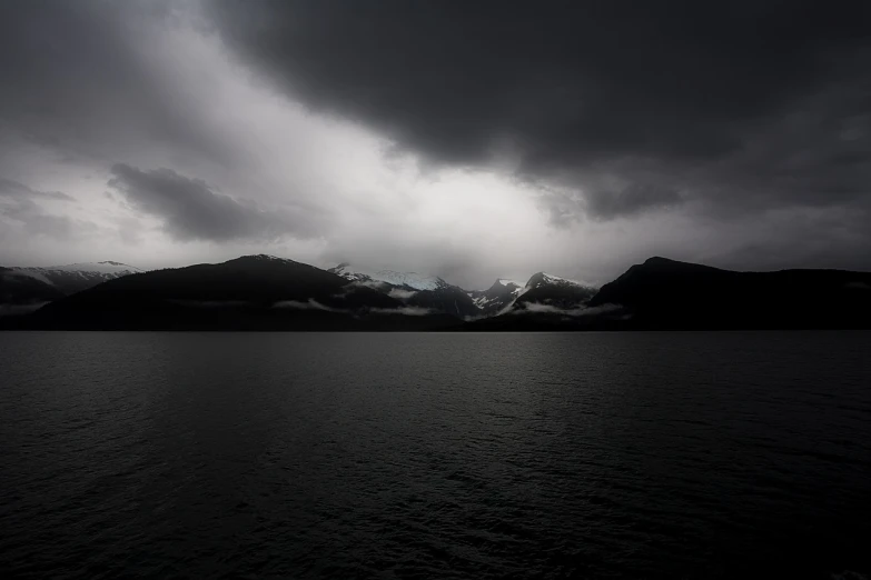 a large body of water with mountains in the background, a picture, inspired by Ansel Adams, minimalism, ominous nighttime storm, snowy fjord, taken with a pentax k1000, light and dark