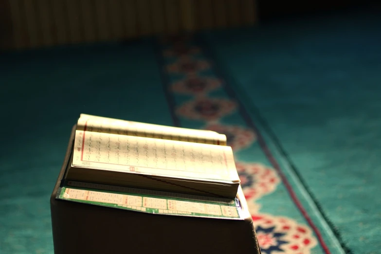 a stack of books sitting on top of a blue carpet, by Sheikh Hamdullah, flickr, hurufiyya, notebook, evening sunlight, mosque interior, [ [ hyperrealistic ] ]