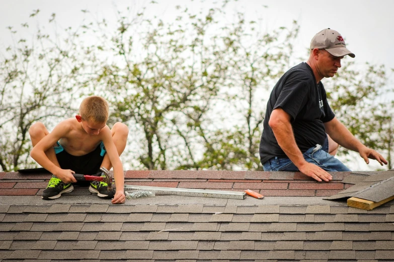 a couple of men sitting on top of a roof, by Joe Stefanelli, pexels, happening, with a kid, repairing the other one, iowa, usa-sep 20