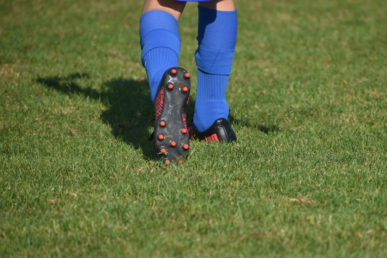 a person standing on top of a lush green field, 1 red shoe 1 blue shoe, wearing a school soccer uniform, close-up shot taken from behind, little kid