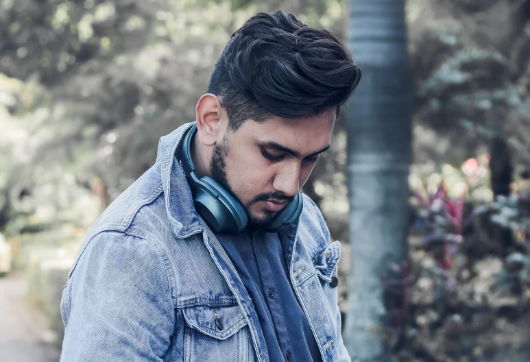 a man wearing headphones looking down at his phone, a portrait, inspired by Nadim Karam, shutterstock, wearing a jeans jackets, black to blue fade hairstyle, cinematic outfit photo, portait photo profile picture