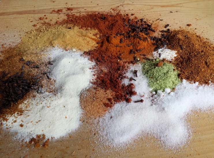 a pile of spices sitting on top of a wooden table, inspired by Tilo Baumgärtel, tumblr, flour dust spray, dark brown white green colours, red sand, on a bright day