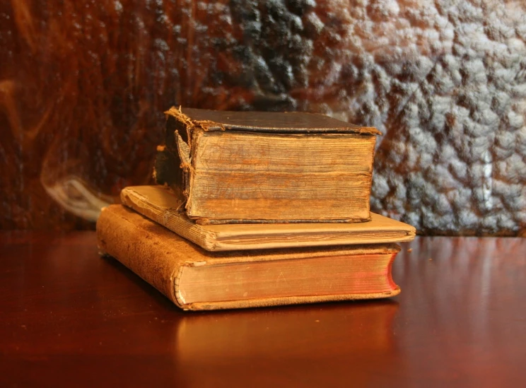 a stack of old books sitting on top of a wooden table, by Robert Brackman, vanitas, wikimedia commons, bark, trio, brown