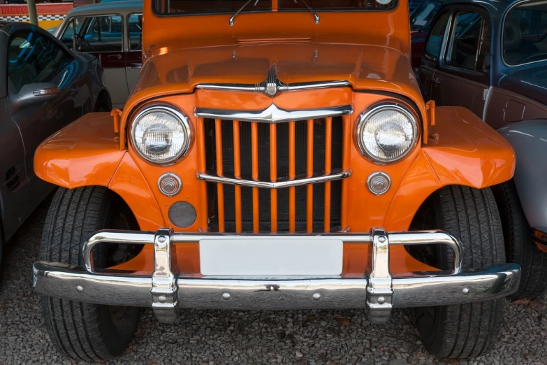 an orange jeep is parked next to other cars, a photo, by Jesper Knudsen, shutterstock, photorealism, front face, classic chrome, 🦩🪐🐞👩🏻🦳, frontlight