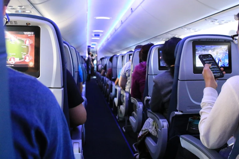 a group of people sitting next to each other on an airplane, a picture, by Matt Cavotta, glowing blue interior components, seen from far away, standing straight, panorama shot