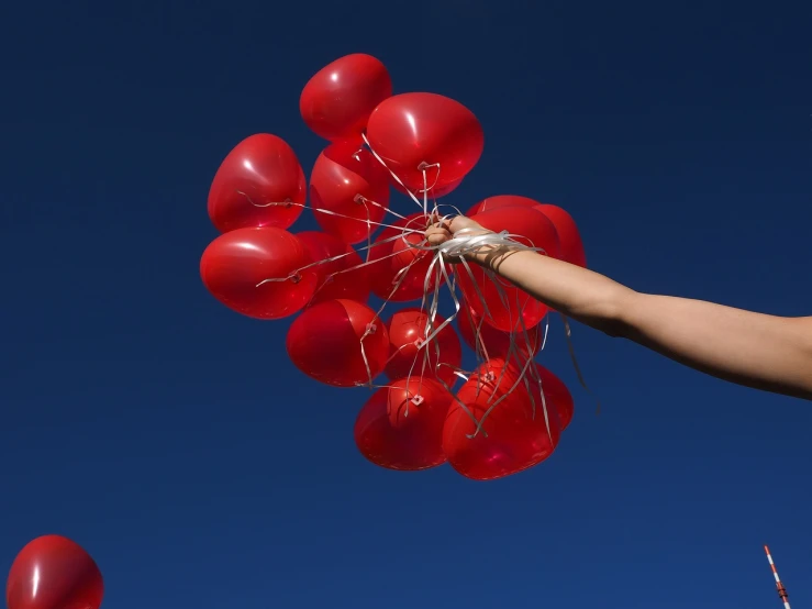 a person holding a bunch of red balloons, by Steven Belledin, happening, cloudless sky, closeup photo, of letting go, hero shot