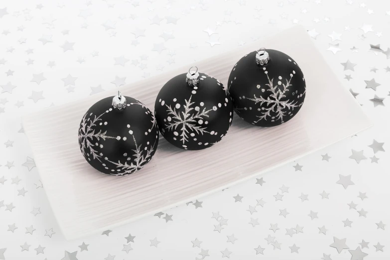 three black and white ornaments on a white plate, miniature product photo