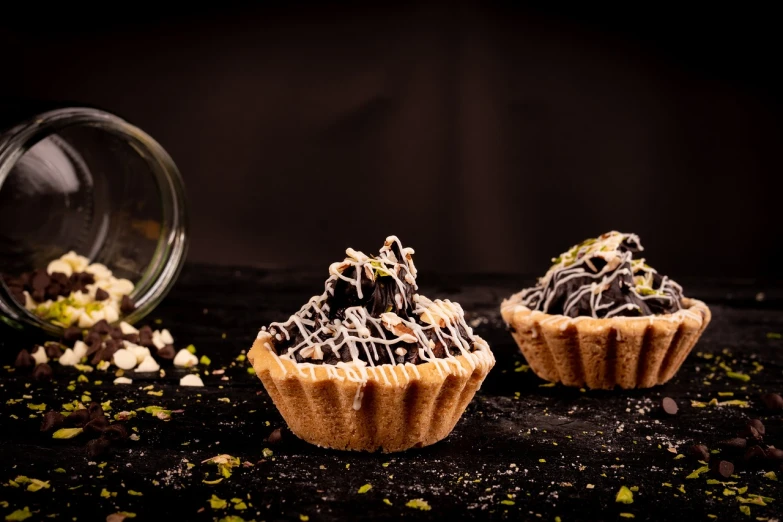 a couple of cupcakes sitting on top of a table, by Aleksander Gierymski, shutterstock, surrealism, with a black dark background, stroopwaffel, highly detailed product photo, foodphoto