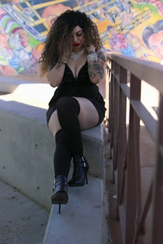 a woman sitting on a ledge talking on a cell phone, a portrait, inspired by Nan Goldin, tumblr, alluring plus sized model, wearing gothic accessories, thigh highs, with long curly hair