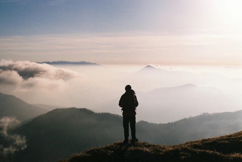 a person standing on top of a hill, a picture, by Karl Buesgen, mountains in fog background, gazing off into the horizon, gradins view, looking in front