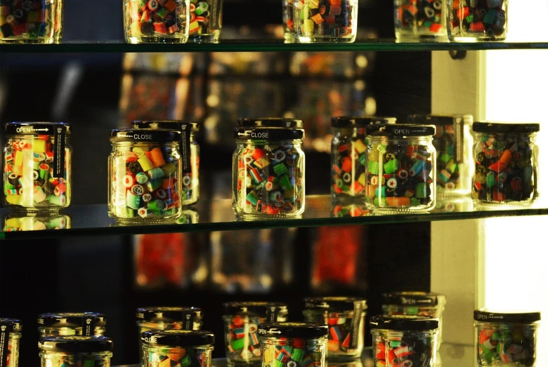 a glass shelf filled with lots of different colored candies, a tilt shift photo, by Aleksander Gierymski, maximalism, large jars on shelves, eyeballs intricated, bracelets, bangalore