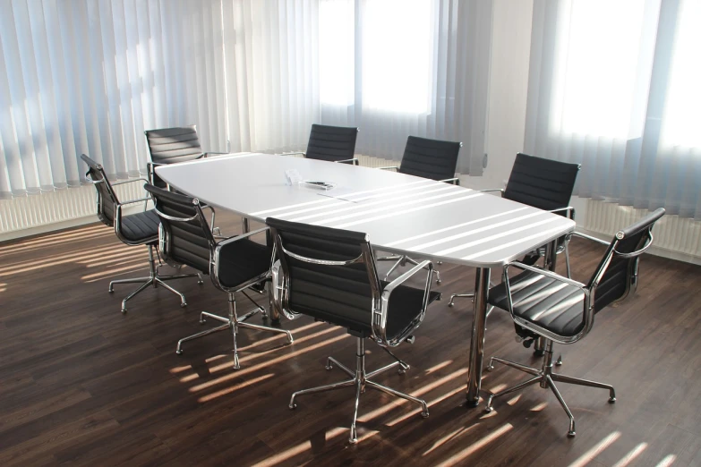 a conference table with chairs and a laptop on it, by Juergen von Huendeberg, pexels, bauhaus, sun beam, white panels, chromed metal, ground-level view