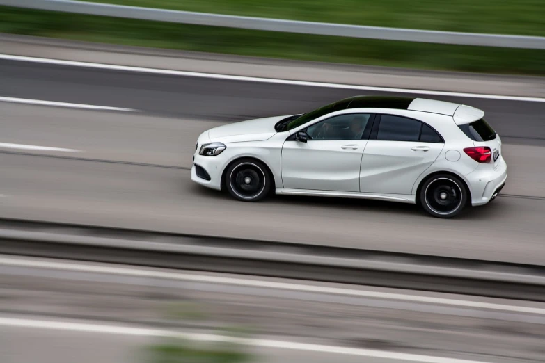 a white car is driving down the road, a picture, by Alexander Brook, aerodynamic body, mercedez benz, shot from the side, panoramic