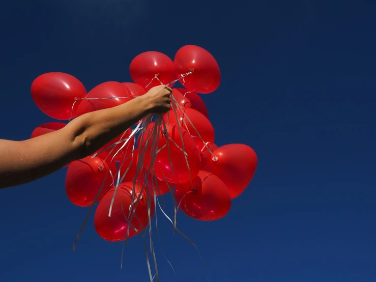 a person holding a bunch of red balloons, by Steven Belledin, happening, blue sky, a close-up, skins, hero shot