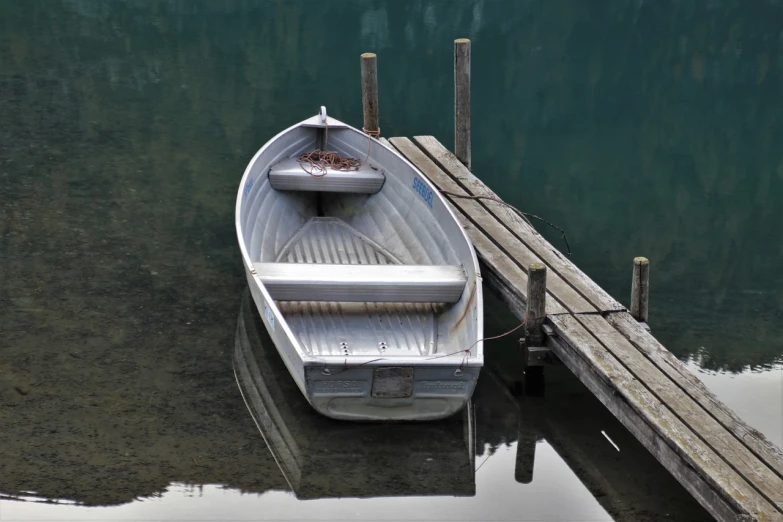 a boat sitting on top of a lake next to a dock, a photo, by Jim Nelson, shutterstock, grey metal body, dingy, half body photo, stock photo