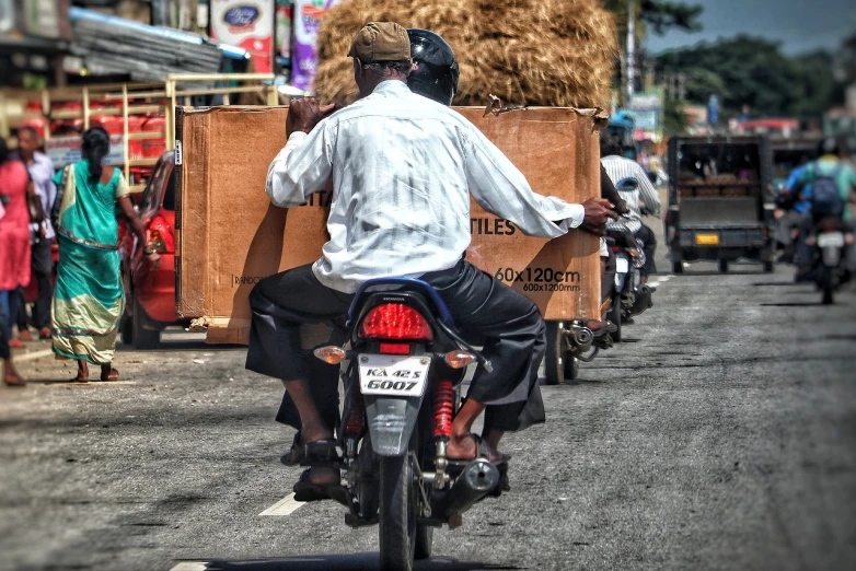 a man riding on the back of a motorcycle down a street, by Richard Carline, flickr, sri lanka, cardboard, highly contrasted elements, people at work