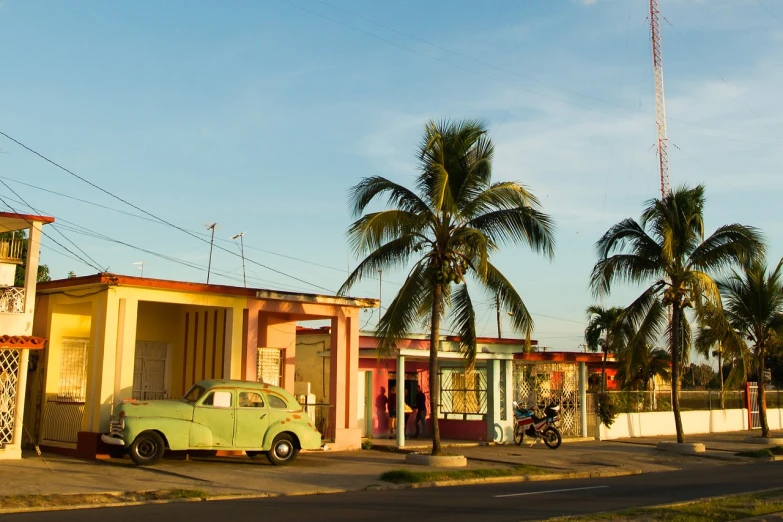 a green car parked on the side of a road, flickr, art deco, varadero beach, small houses, warm sundown, dried palmtrees