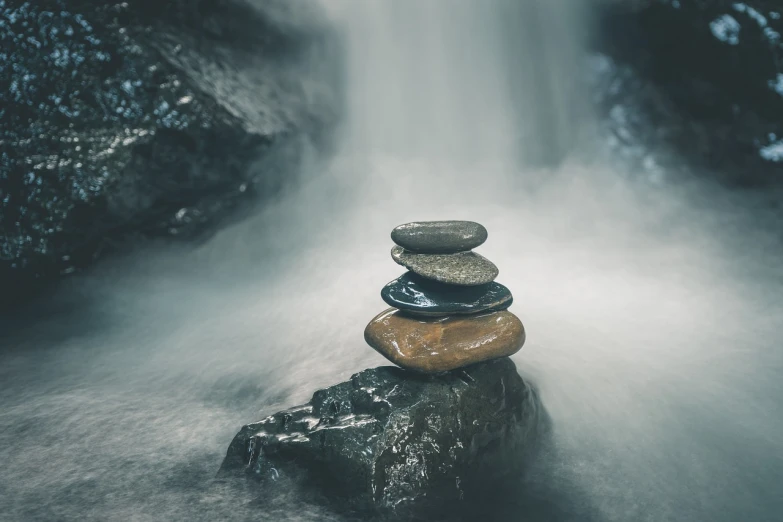 a pile of rocks sitting on top of a rock in front of a waterfall, minimalism, floating in a misty daze, 5 5 mm photo
