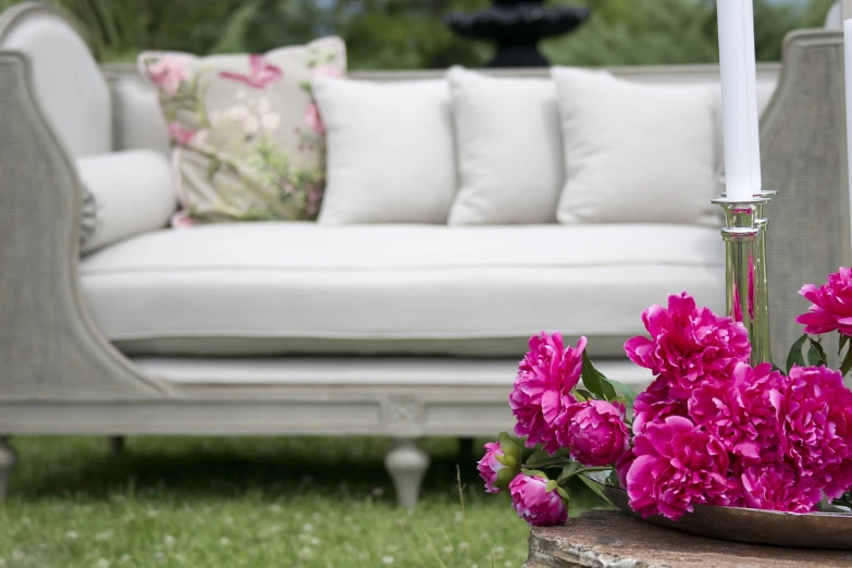 a white couch sitting on top of a lush green field, inspired by Pierre-Joseph Redouté, baroque, peony flowers, beautiful high detail photo, garden setting, magenta and gray