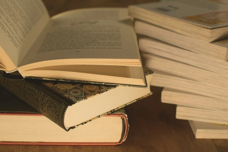 a stack of books sitting on top of a wooden table, by Maksimilijan Vanka, pixabay, figuration libre, bottom angle, cinematic close shot, hyperrealistic composition, product introduction photo