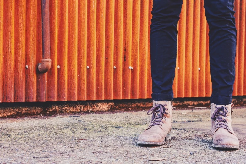 a person standing in front of a red wall, by Karl Buesgen, wears brown boots, vintage saturation, background focus, cargo pants