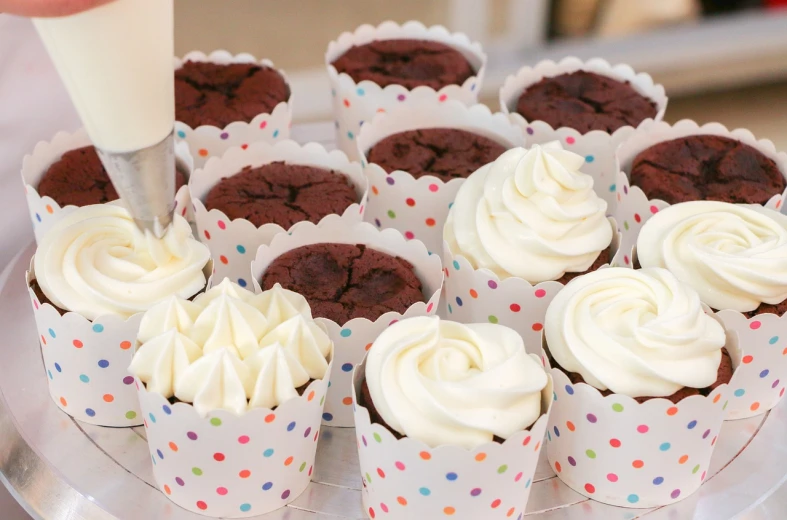 a close up of a plate of cupcakes with frosting, by Lorraine Fox, event photography, white with chocolate brown spots, polka dot tables, closeup - view