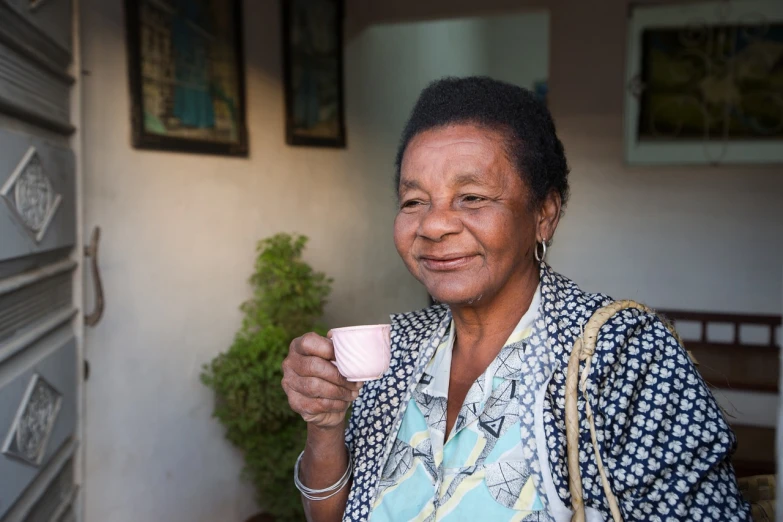 a woman holding a cup of coffee in her hand, a portrait, by Willian Murai, 70 years old, cuban setting, african woman, portrait mode photo