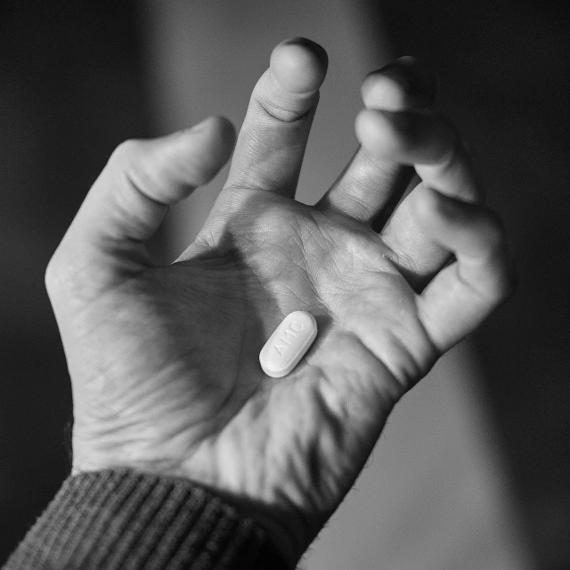 a person holding a pill in their hand, a black and white photo, by Adam Chmielowski, wikimedia, très détaillé, moderately detailed, holding a pudica pose