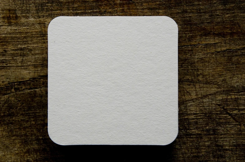 a piece of paper sitting on top of a wooden table, inspired by Kazimir Malevich, rounded corners, 5 5 mm photo, back facing the camera, white: 0.5