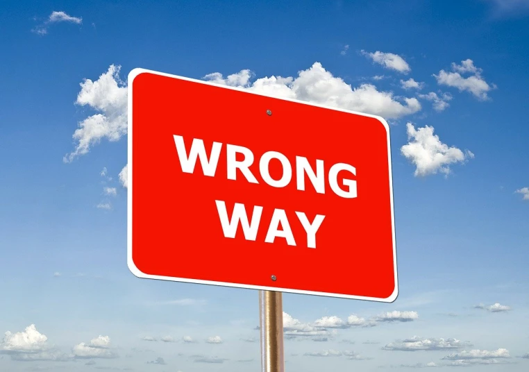 a red wrong way sign sitting on the side of a road, a picture, istockphoto, some edges lost, hovering indecision, awingawat