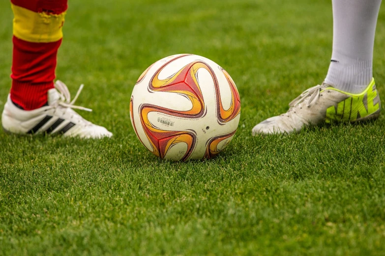 a soccer ball sitting on top of a lush green field, a picture, by Christen Dalsgaard, focus on his foot, sports logo, godes, cups and balls