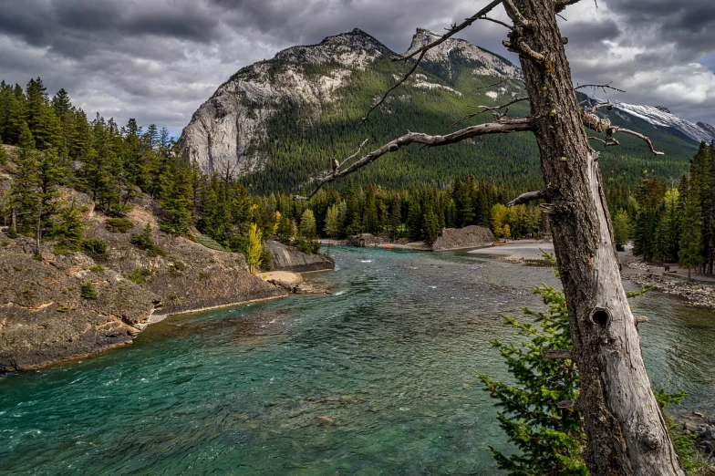 a view of a river with a mountain in the background, by Raymond Normand, shutterstock, process art, banff national park, deep colours. ”, menacing!!!, river and trees and hills