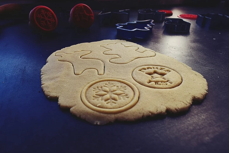 a cookie sitting on top of a table next to cookie cutters, inspired by Rudolph Belarski, pixabay, folk art, cyberpunk ornaments, stamp, 33mm photo, video game dunkey
