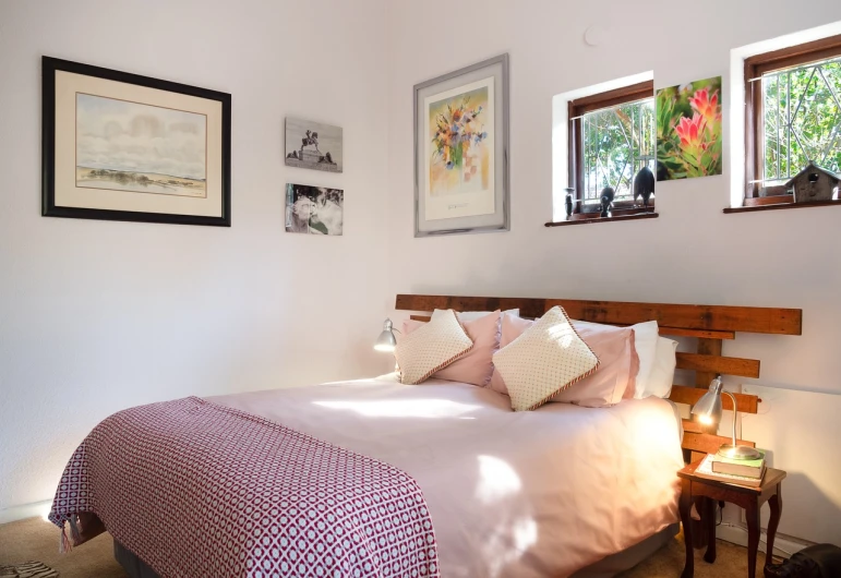 a bed room with a neatly made bed and pictures on the wall, a portrait, cottage, brightly lit pink room, afternoon sunshine, cape