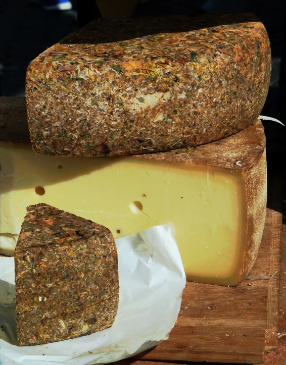 a pile of cheese sitting on top of a wooden cutting board, by Erwin Bowien, renaissance, view from the side, hay, speckled, amber