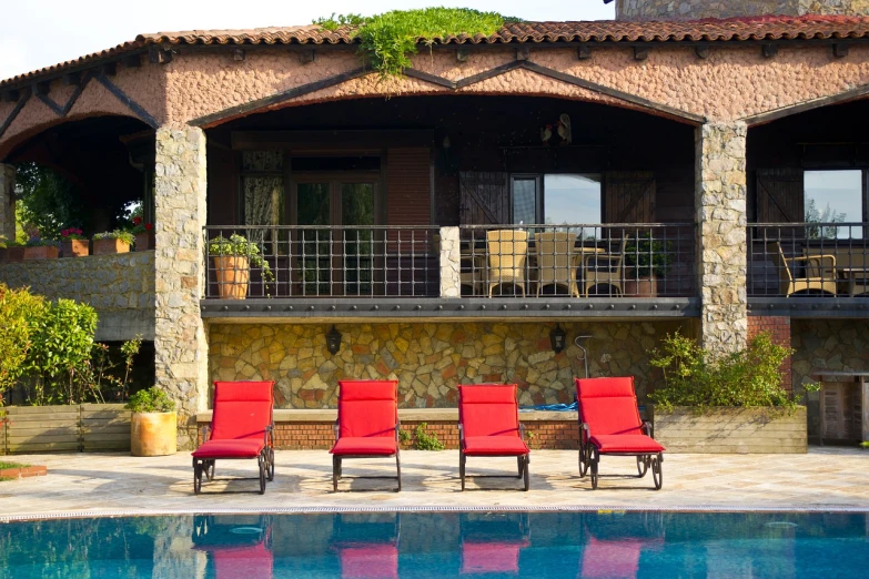 a couple of red chairs sitting next to a swimming pool, shutterstock, stone roof, superior detail, hillside, laura sava