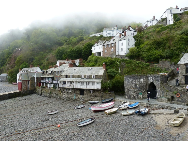 a group of boats sitting on top of a rocky beach, a picture, pexels, plein air, medieval tumbledown houses, mist below buildings, uk, thatched roofs