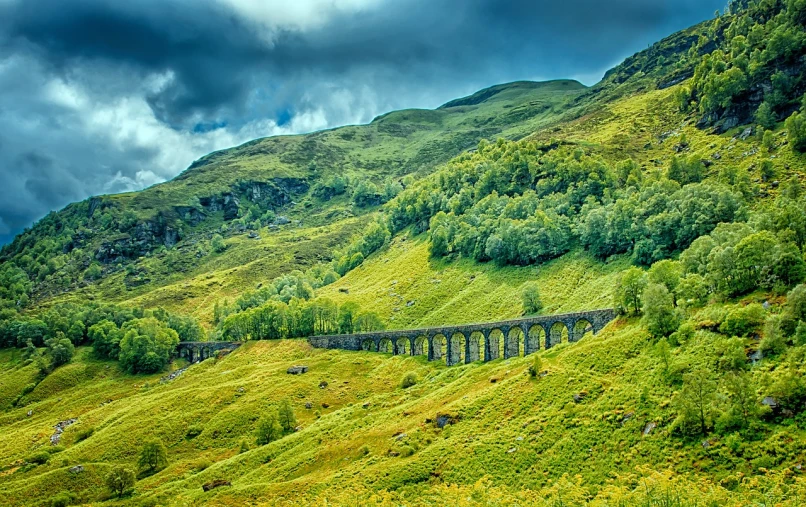 a train traveling through a lush green hillside, by Andrew Robertson, shutterstock, stone walls and pillars, fairyland bridge, overcast weather, highlands