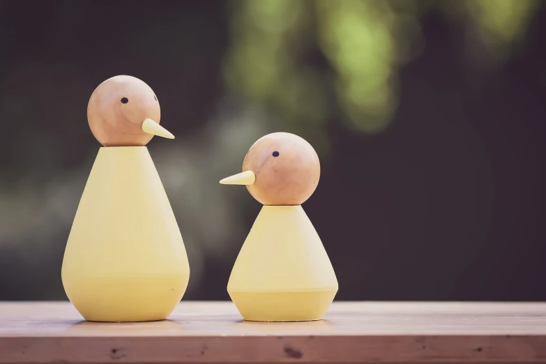 a couple of wooden ducks sitting on top of a wooden table, a picture, inspired by Jacob Duck, pexels, minimalism, glossy yellow, cute boys, petite pear slim figure, cone heads