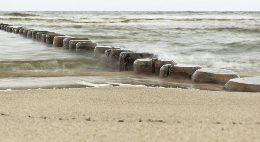 a group of rocks sitting on top of a sandy beach, a picture, inspired by Tom Wänerstrand, plasticien, sleepers, water line surface, close-up product photo, blowing sands