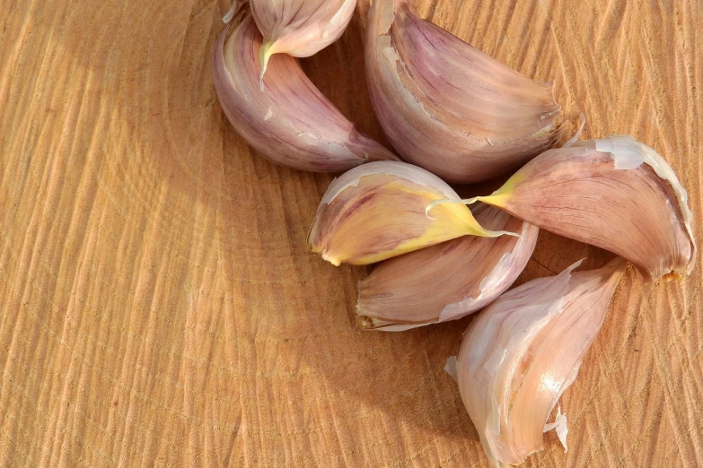 a bunch of garlic sitting on top of a wooden table, a picture, by Tom Carapic, high detail product photo, petals, cooked, close-up product photo