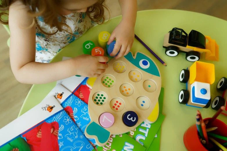 a little girl playing with wooden toys on a table, a picture, process art, colorful fish, children playing with pogs, product introduction photo, mathematical