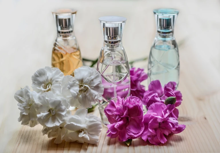 three bottles of perfume sitting on top of a wooden table, by Maksimilijan Vanka, pixabay, with colored flowers, stock photo, carnation, wearing simple robes